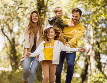 a mom and dad walk happily through a wooded park with their two children